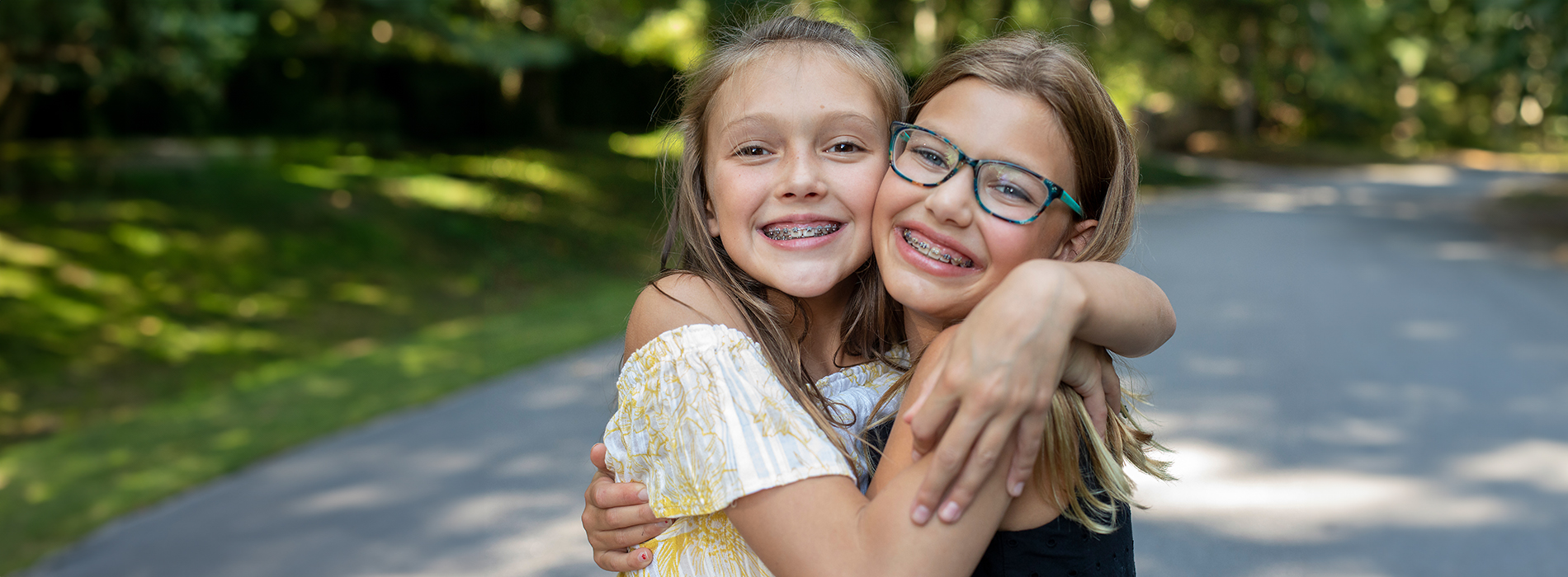 Two young girls hugging each other outdoors during daylight hours.