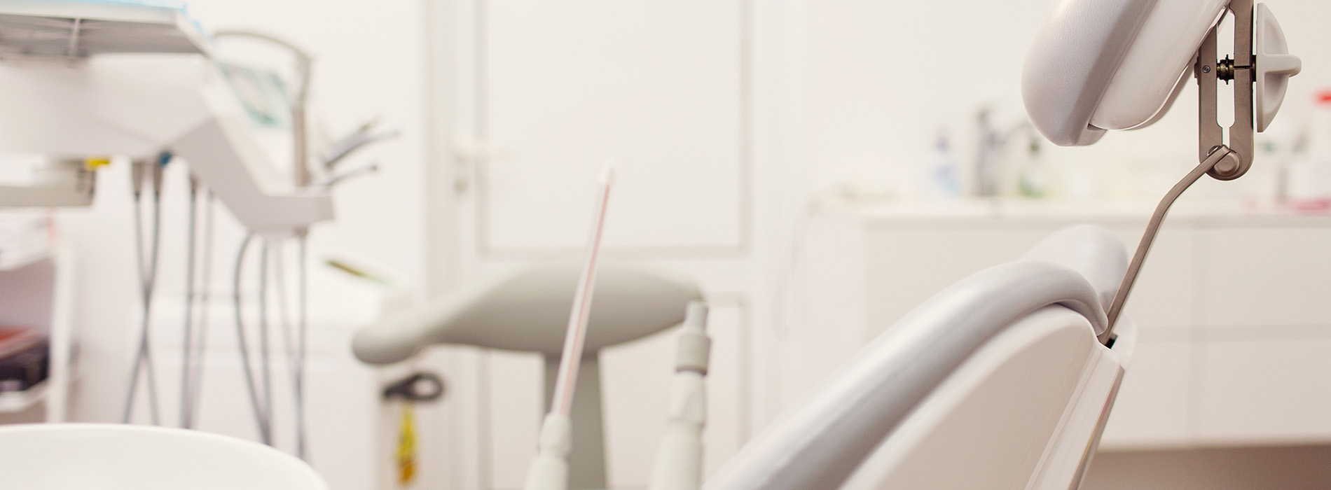 The image shows a dental clinic with a dental chair and equipment in the foreground, and a blurred background showing a dentist s office with a desk and chairs.