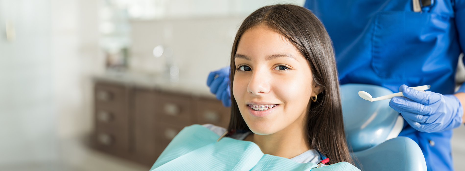 A woman sitting in a dental chair with a hygienist performing a cleaning procedure on her teeth.