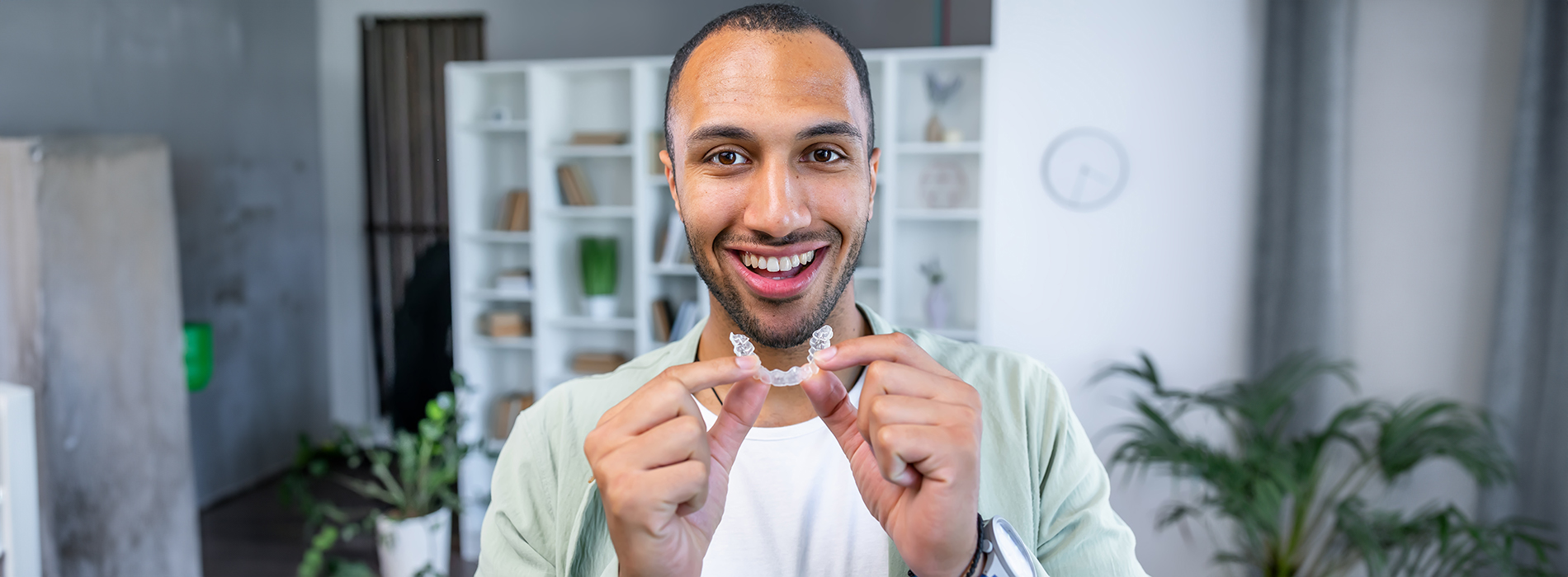 A man holding up two fingers in a peace sign gesture with a smile on his face against a blurred indoor background.