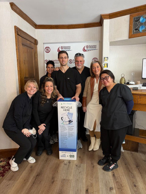 The image shows a group of people standing around a man holding an item with a logo on it, likely at a promotional event or gathering.