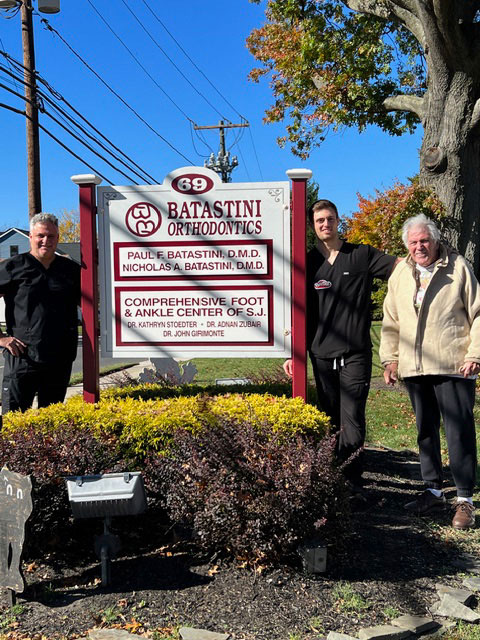 The image features three individuals standing next to a sign with text, posing for a photo outdoors.