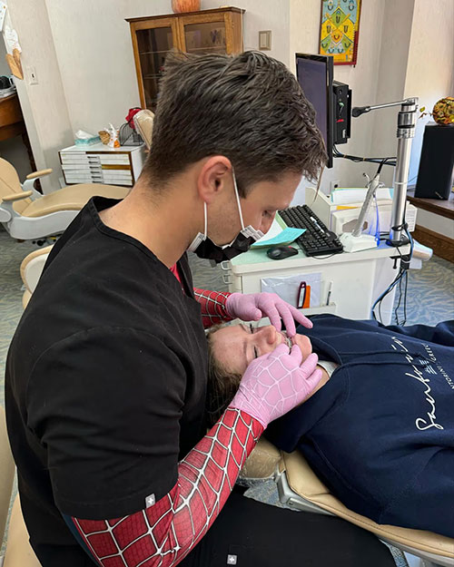 Dentist examining patient s mouth with dental mirror and gloves, both wearing masks in dental office setting.