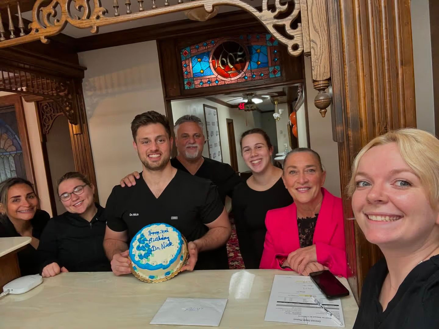 Group of people posing with cake at restaurant, smiling towards camera, celebratory atmosphere.