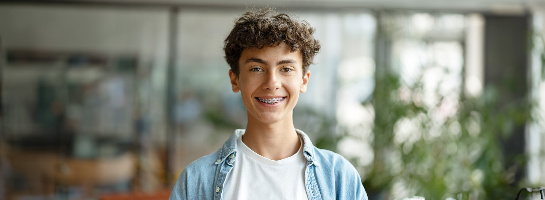 A young man with a smile stands against a blurred background, likely in an indoor setting.