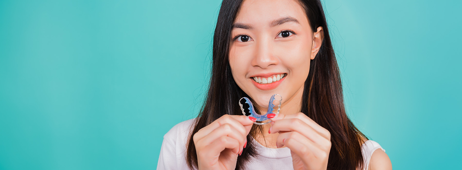 The image shows a woman holding up a small figurine with her right hand, smiling at the camera, against a blue background.