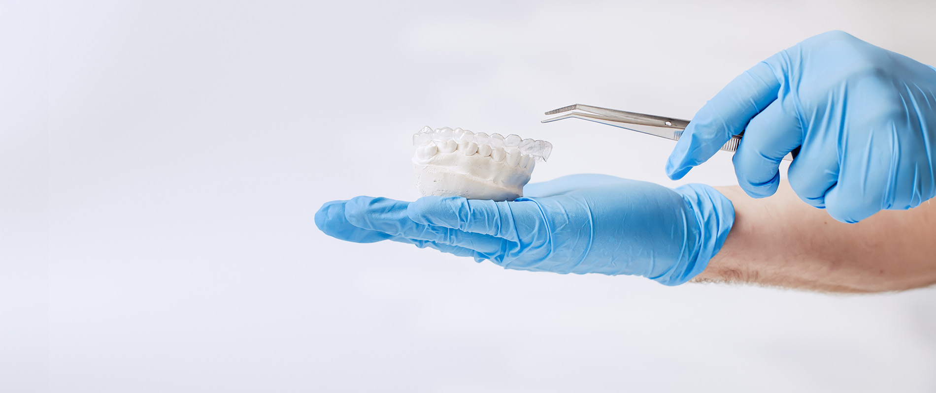 A person s hand wearing blue gloves holds a white object, likely a toothbrush, against a light background.