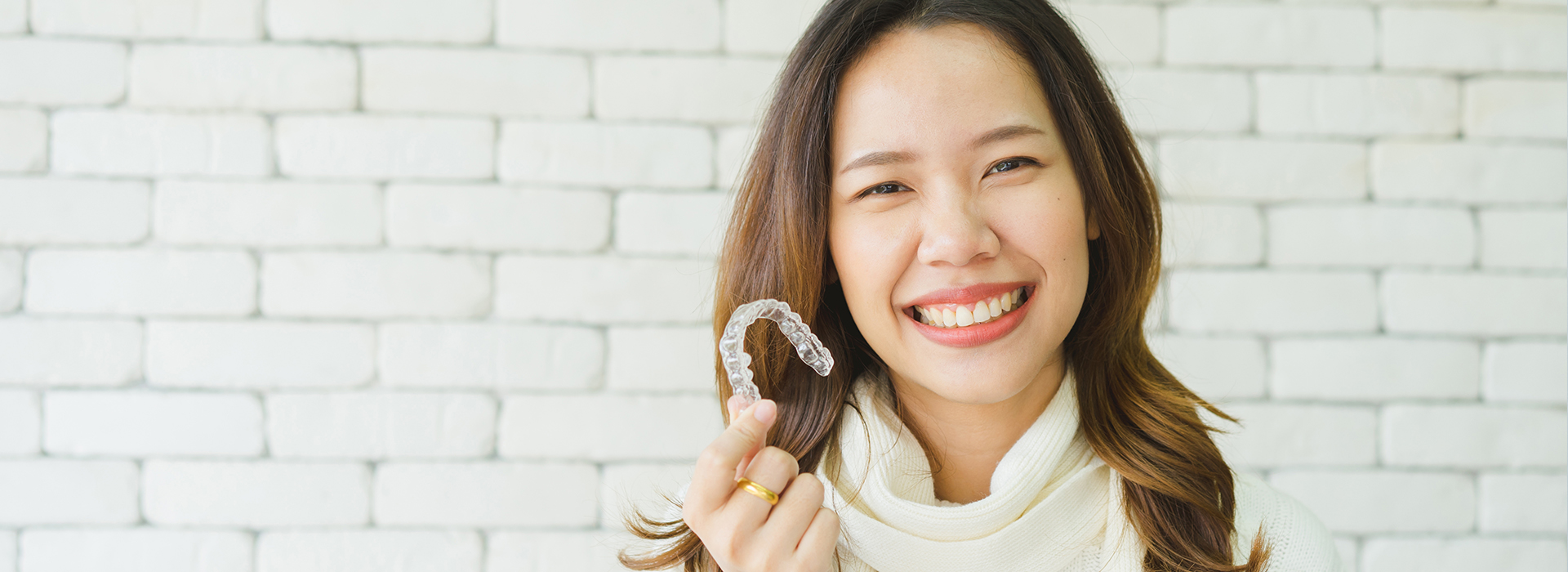 A woman with a big smile holds up a toothbrush against her mouth.
