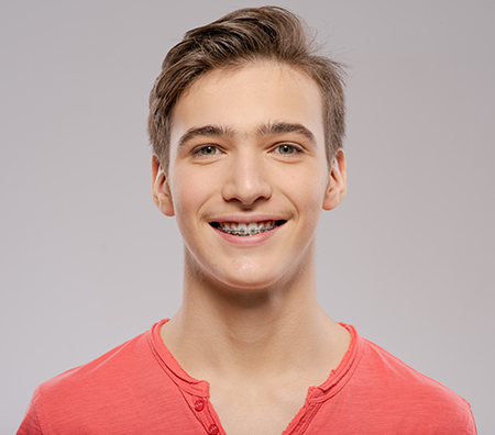 The image shows a young man with a light-colored haircut smiling at the camera against a plain background.