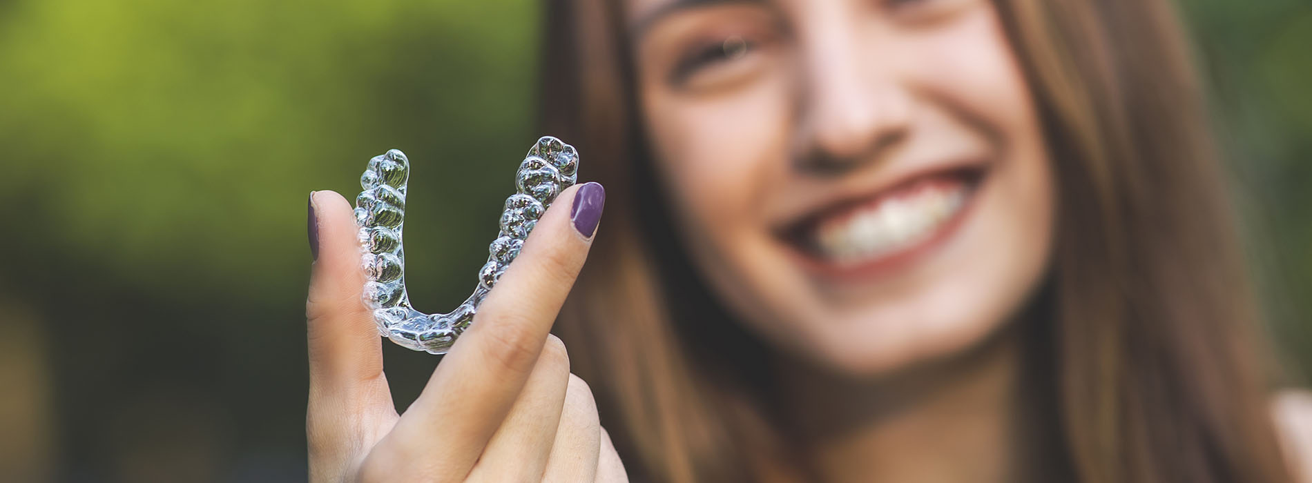 The image shows a person holding up a hand with a clear plastic object shaped like a heart, smiling at the camera.